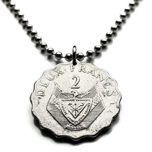 May include: A silver-colored necklace featuring a vintage Deux Francs coin pendant. The coin has a scalloped edge and features the number 2, text, and an emblem. The necklace chain is made of small, round, silver-colored beads.