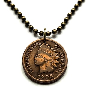 May include: A copper-colored Indian Head penny pendant necklace. The coin, dated 1906, features a profile of a Native American in a feathered headdress. The necklace has a bronze-colored ball chain.