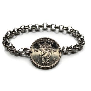 Puede incluir: Una pulsera de plata con un dije de moneda noruega de 1 corona de 1954. La moneda presenta el escudo de armas noruego y la inscripción "NORGE 1 KRONER".