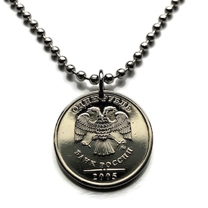 May include: A silver-toned necklace featuring a coin pendant. The coin displays a double-headed eagle emblem and Cyrillic text. The year "2005" is visible on the coin. The necklace has a ball chain.