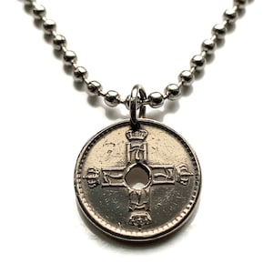 Puede incluir: Collar plateado con un colgante de moneda. El colgante presenta un diseño de cruz con un agujero central y detalles intrincados. La cadena está hecha de pequeñas cuentas redondas.