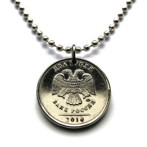 May include: A silver-colored coin pendant necklace. The coin features a double-headed eagle emblem and Cyrillic text. The necklace chain is made of small, round, silver-colored beads. The coin is dated 2010.