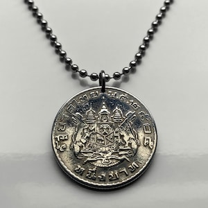 Puede incluir: Un collar de plata con un colgante que presenta una moneda tailandesa con el escudo de armas real y texto tailandés. La moneda está rodeada por una cadena de plata.