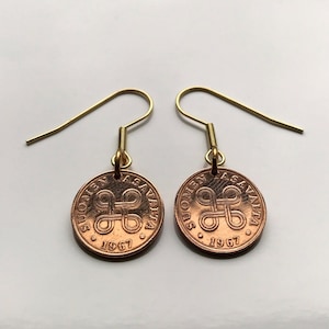 Op de afbeelding: Een paar gouden oorringen met Finse koperen munten uit 1967. De munten dragen de tekst "Suomen Tasavalta" en een gestileerd knoopontwerp.