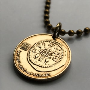 Puede incluir: Collar de oro con un colgante redondo que presenta un árbol y la inscripción "ישראל" en hebreo. El colgante está unido a una cadena de oro.