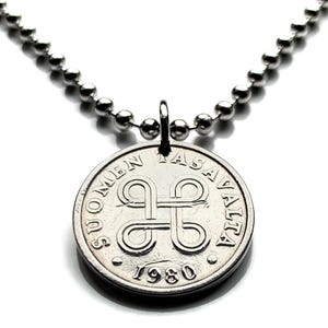 Op de afbeelding: Een zilverkleurige ketting met een ronde hanger. De hanger is een munt met de tekst "SUOMEN TASAVALTA" en het jaartal "1980". De ketting bestaat uit kleine, ronde kralen.