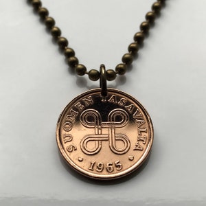Op de afbeelding: Een ketting met een koperkleurige munt en een ketting van kleine, ronde, bronzen kralen. De munt heeft de tekst "SUOMEN ASAVALTA" en het jaar "1965" rond een gestileerd knoopontwerp.