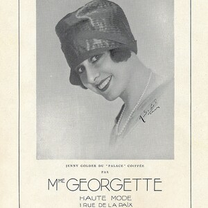 Puede incluir: Una fotografía en blanco y negro de una mujer con un sombrero negro y un collar de perlas. El texto "JENNY GOLDER DU 'PALACE' COIFFÉE PAR MME GEORGETTE HAUTE MODE 1 RUE DE LA PAIX PARIS" está impreso debajo de la fotografía.
