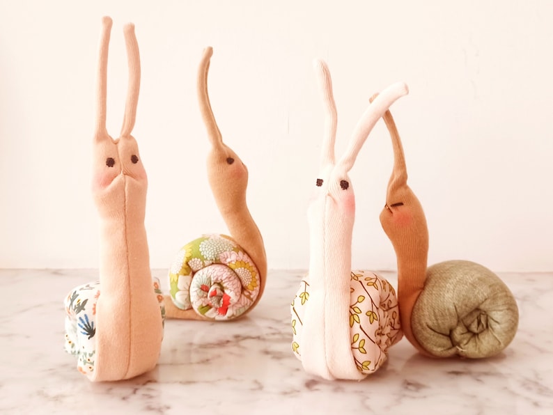 May include: Four handmade fabric snails in different colors and patterns. The snails are made from soft fabric and have embroidered eyes. They are a fun and whimsical addition to any home decor.