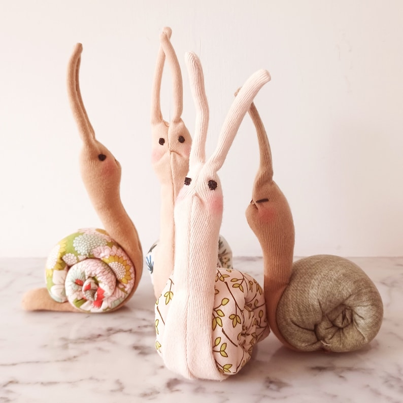 May include: Three handmade fabric snail toys. One snail is pink with a floral pattern, one is brown with a floral pattern, and one is green.