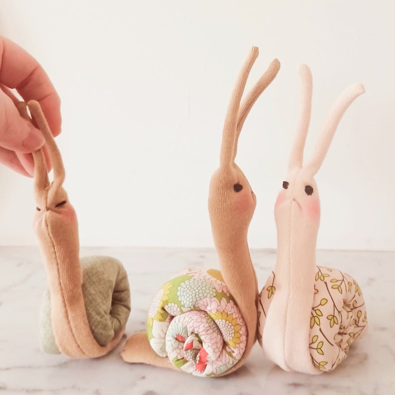 May include: Three handmade fabric snail toys. One is brown with a green shell, one is brown with a floral shell, and one is pink with a green and brown leaf patterned shell.