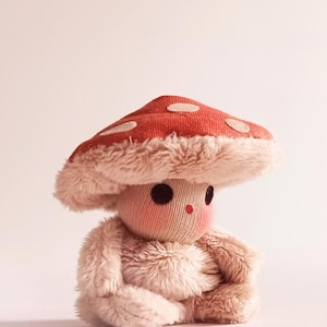 May include: A plush toy shaped like a mushroom with a red and white polka dot cap and a soft, fuzzy body.