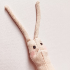 May include: A beige fabric bunny with long ears and black eyes. The bunny has pink cheeks.