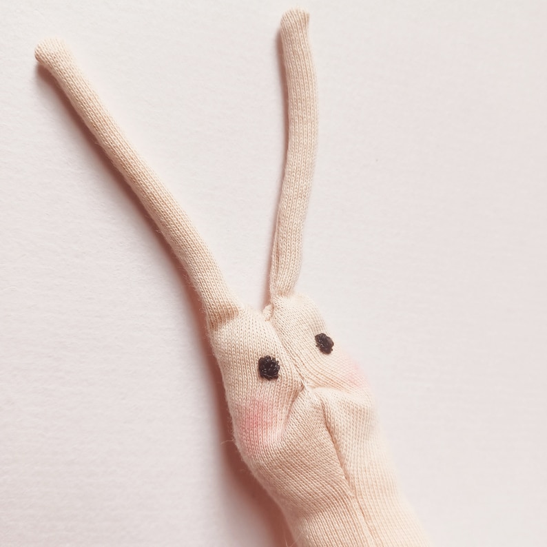 May include: A beige fabric bunny with long ears and black eyes. The bunny has pink cheeks.