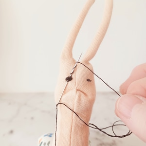 May include: A close-up of a light pink fabric snail with black eyes being sewn with a needle and black thread. The snail is sitting on a fabric with a floral pattern.