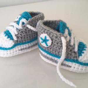 May include: A pair of gray and white crocheted baby booties with blue accents and a white star on one bootie.