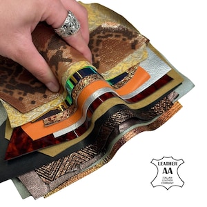 May include: A collection of stacked leather swatches in various textures and colours, including brown snake print, metallic silver, bright orange, black, and iridescent finishes. A logo in the corner reads LEATHER AA ITALIAN LEATHER COMPANY.