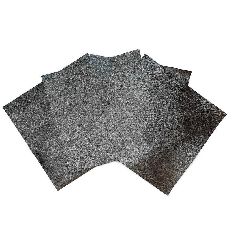 May include: A collection of five dark gray sheets of textured material, fanned out against a white background. The sheets have a slightly rough, speckled appearance, suggesting a metallic or glittery finish. The edges are clean and defined.