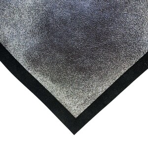 May include: A silver, textured material with a black border, forming a corner shape. The silver surface has a mottled appearance, and the black border is a solid, dark color. The contrast between the two materials is striking.
