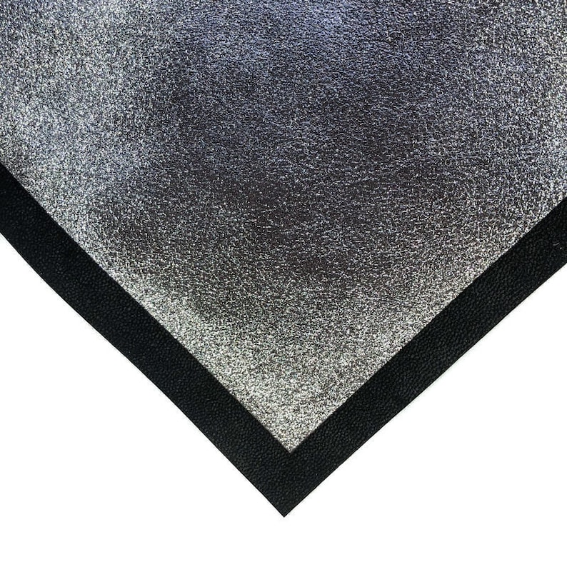 May include: A silver, textured material with a black border, forming a corner shape. The silver surface has a mottled appearance, and the black border is a solid, dark color. The contrast between the two materials is striking.