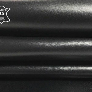 May include: Close-up of black leather folded in layers. The leather has a smooth, slightly textured surface. A white label with the text "LEATHER AA ITALIAN LEATHER COMPANY" is visible in the top left corner.