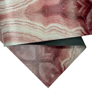 Puede incluir: Primer plano de un material texturizado con un patrón veteado en tonos burdeos, rosa y blanco. El material está doblado, revelando un reverso gris oscuro. El efecto general recuerda a la piedra natural o la veta de la madera.