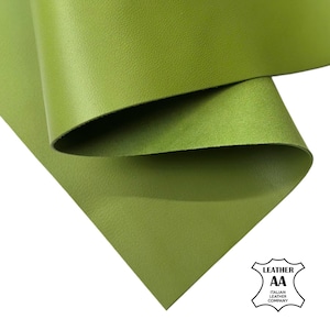 Puede incluir: Primer plano de una hoja de cuero verde oliva, con una textura sutil y un ligero brillo. El cuero está doblado, revelando la parte inferior. El logotipo de Italian Leather Company está en la esquina inferior derecha.