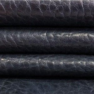 May include: Close-up of dark navy blue leather. The leather has a textured, wrinkled appearance, with visible grain and subtle variations in color. The image shows several layers of the material.