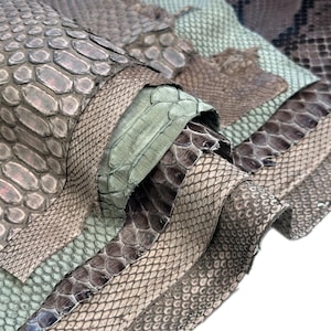 Puede incluir: Primer plano de varios trozos de piel de serpiente en varios tonos de gris, marrón y verde. Las pieles están superpuestas y enrolladas, mostrando las escamas texturizadas y los patrones naturales. La imagen destaca los diferentes colores y texturas de las pieles de reptiles.