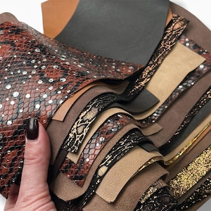 May include: A stack of different colored and patterned leather swatches. The swatches include brown, black, beige, and a snakeskin pattern.