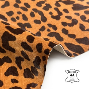 Può includere: Primo piano di un pezzo di pelle con stampa animalier. La pelle ha uno sfondo beige con macchie marroni scure. Il bordo della pelle è ripiegato, rivelando un lato inferiore bianco. Il logo Italian Leather Company si trova nell'angolo in basso a destra.