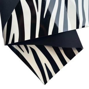 Peut inclure: Un morceau plié de tissu noir avec un motif zébré. L'imprimé zébré présente des rayures noires et blanches, avec quelques rayures grises. Le tissu est plié, révélant un dessous noir uni.