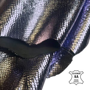May include: Close-up of a sheet of iridescent, textured leather. The leather has a scale-like pattern and reflects shades of purple, silver, and gold. The image includes a logo for an Italian leather company.