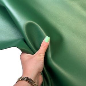 Puede incluir: Un material verde bosque sólido y liso con un acabado mate. La superficie es flexible y maleable, mostrando pliegues y curvas suaves. El material tiene un color verde profundo y consistente en toda su extensión, con una textura uniforme.