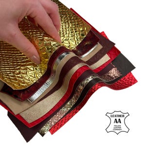 Puede incluir: Una mano sosteniendo una selección de muestras de cuero en varios colores y texturas. Las muestras incluyen tonos dorados, rojos, plateados y marrones, algunas con patrones en relieve. La imagen incluye el logotipo de Italian Leather Company.