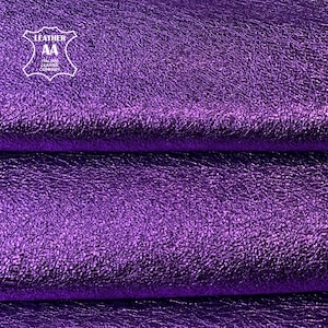 May include: Close-up of a textured, metallic purple leather. The leather is folded, revealing the grain and sheen. The image includes a white logo that reads "LEATHER AA ITALIAN LEATHER COMPANY".