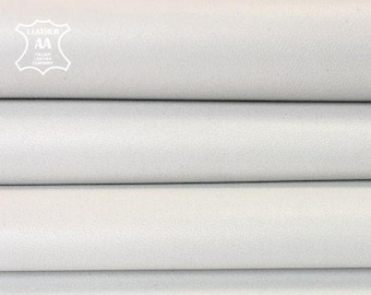 May include: A stack of folded white leather sheets with a smooth, matte texture. In the top left corner, a white emblem features the text LEATHER AA ITALIAN LEATHER COMPANY inside a stylized hide shape, indicating the material origin.