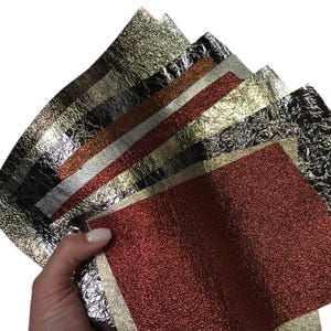 May include: A collection of rectangular sheets of metallic material in various colors including gold, silver, copper, and deep red. Each sheet features a distinct crinkled, textured surface finish that reflects light, layered together in a fan shape.
