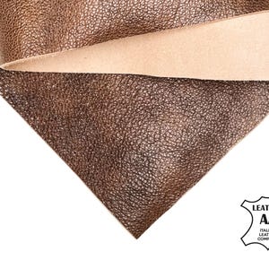 May include: Close-up of brown leather with a textured surface. The leather is folded over, revealing a lighter tan underside. The image includes a logo that says "LEATHER AA ITALIAN LEATHER COMPANY".