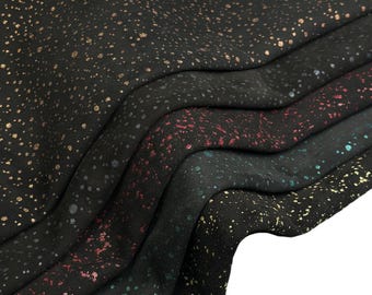 Puede incluir: Una colección de capas de tela negra con un patrón moteado y acentos metálicos en dorado, rojo y turquesa. El material está drapeado en pliegues suaves y ondulados, mostrando la densa distribución de puntos brillantes sobre la superficie oscura.