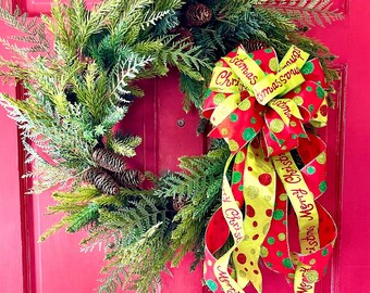 Pode incluir: Uma guirlanda de Natal verde com pinhas e uma fita vermelha e amarela com o texto "Feliz Natal" e "Feliz Ano Novo" nela. A guirlanda está pendurada em uma porta rosa brilhante.