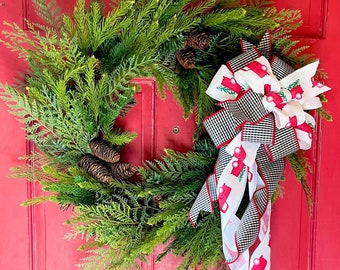 Pode incluir: Uma guirlanda de Natal verde com pinhas e uma fita vermelha e branca com um padrão de caminhão. A guirlanda está pendurada em uma porta vermelha.