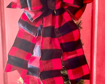 Pode incluir: Um laço de xadrez vermelho e preto com uma textura grande e fofa. O laço está amarrado no topo de uma pequena árvore de Natal artificial.