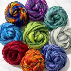 May include: Nine colorful bundles of wool roving, arranged in a circular pattern. The colors include shades of blue, green, purple, red, orange, and yellow. The wool is tightly spun, creating a textured appearance, ideal for fiber art projects.