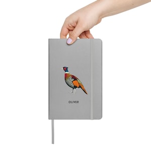 May include: A gray notebook with a colorful pheasant illustration and the name "Oliver" printed on the cover.