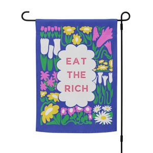 May include: A blue garden flag featuring a white cloud with the text "EAT THE RICH" in pink lettering. The cloud is surrounded by colourful flowers and leaves.
