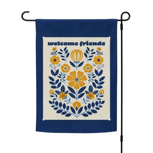 Puede incluir: Una bandera de jardín azul con un borde blanco y un diseño floral en amarillo y azul. El texto "welcome friends" está impreso en blanco en la bandera.
