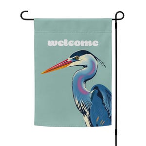 May include: A blue and white garden flag with a welcome message and a colorful illustration of a heron.