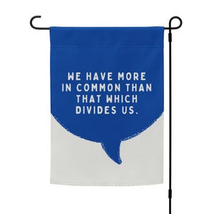 May include: A blue and white garden flag with the text "We have more in common than that which divides us." in a white speech bubble.