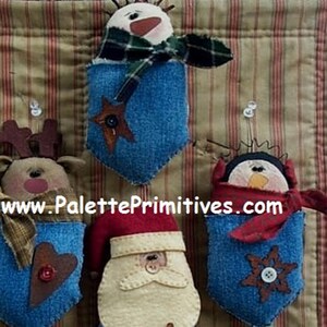 Può includere: Quattro ornamenti natalizi fatti a mano, ognuno con un personaggio diverso: un pupazzo di neve, una renna, Babbo Natale e un pinguino. Ogni ornamento è fatto di tessuto e ha una tasca di jeans blu con un elemento decorativo, come una stella, un cuore, un fiocco di neve o un bottone.